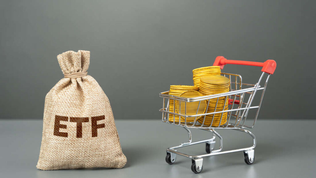 Spielzeug-Einkaufswagen mit Münzen neben einem Geldsack mit der Aufschrift „ETF“ vor grauem Hintergrund.