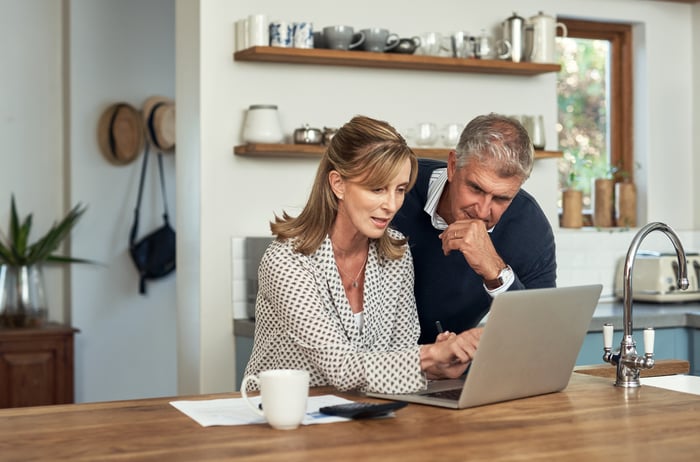 Two people sit at a table and look at a laptop computer together.